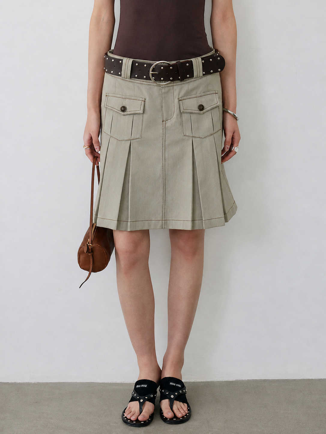 BapHood khaki grey pleated utility skirt with a high waist, belt detail, and front flap pockets.