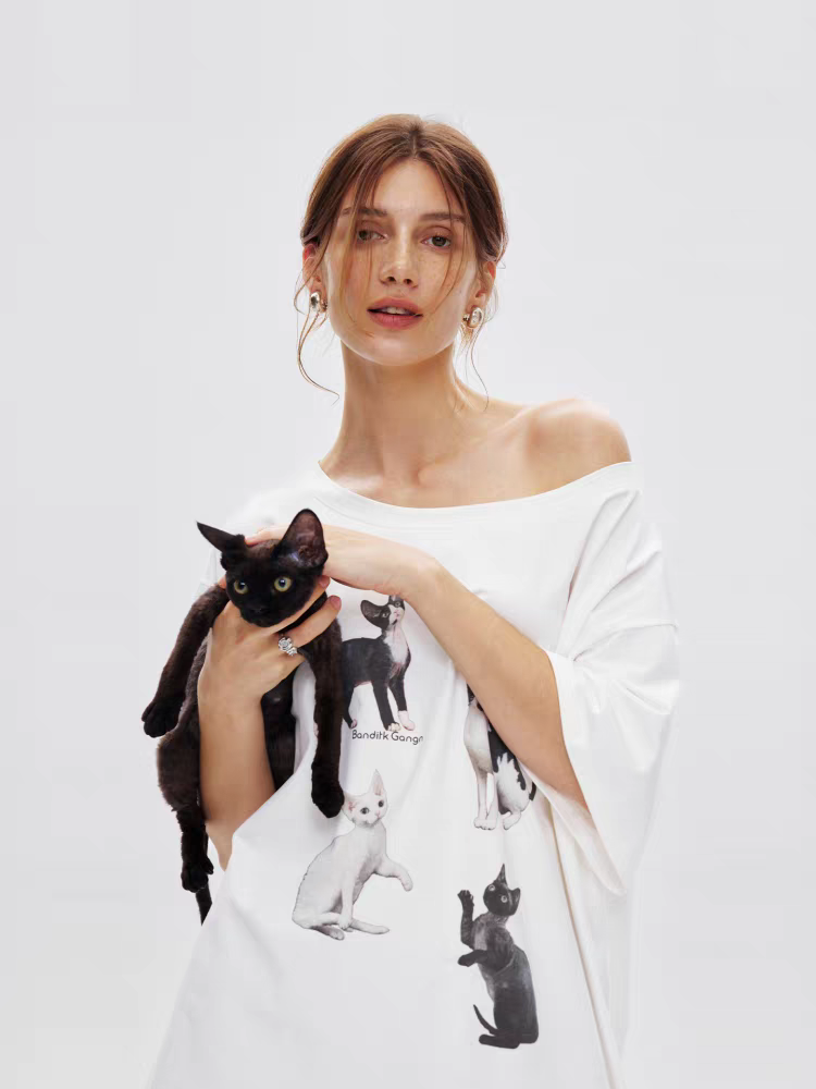 Model wearing white oversized off-shoulder tee dress with kitty gang graphic, front view