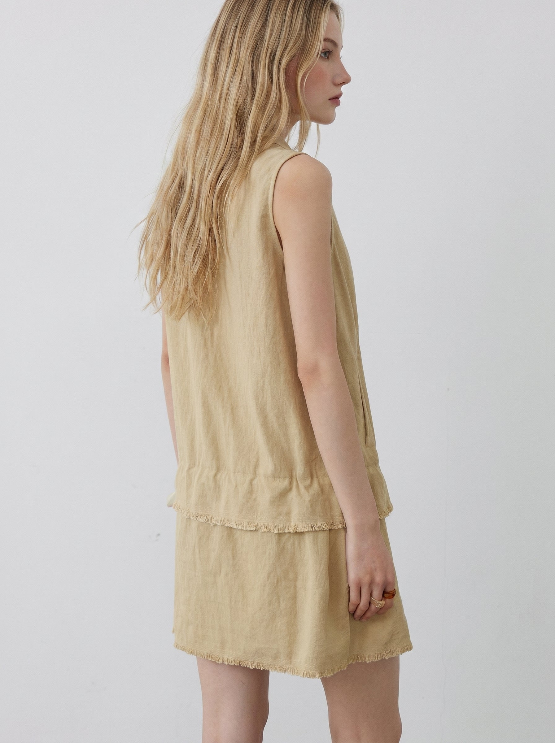 Back view of beige sleeveless mini dress with relaxed sleeveless cut, layered hem, and soft textured fabric