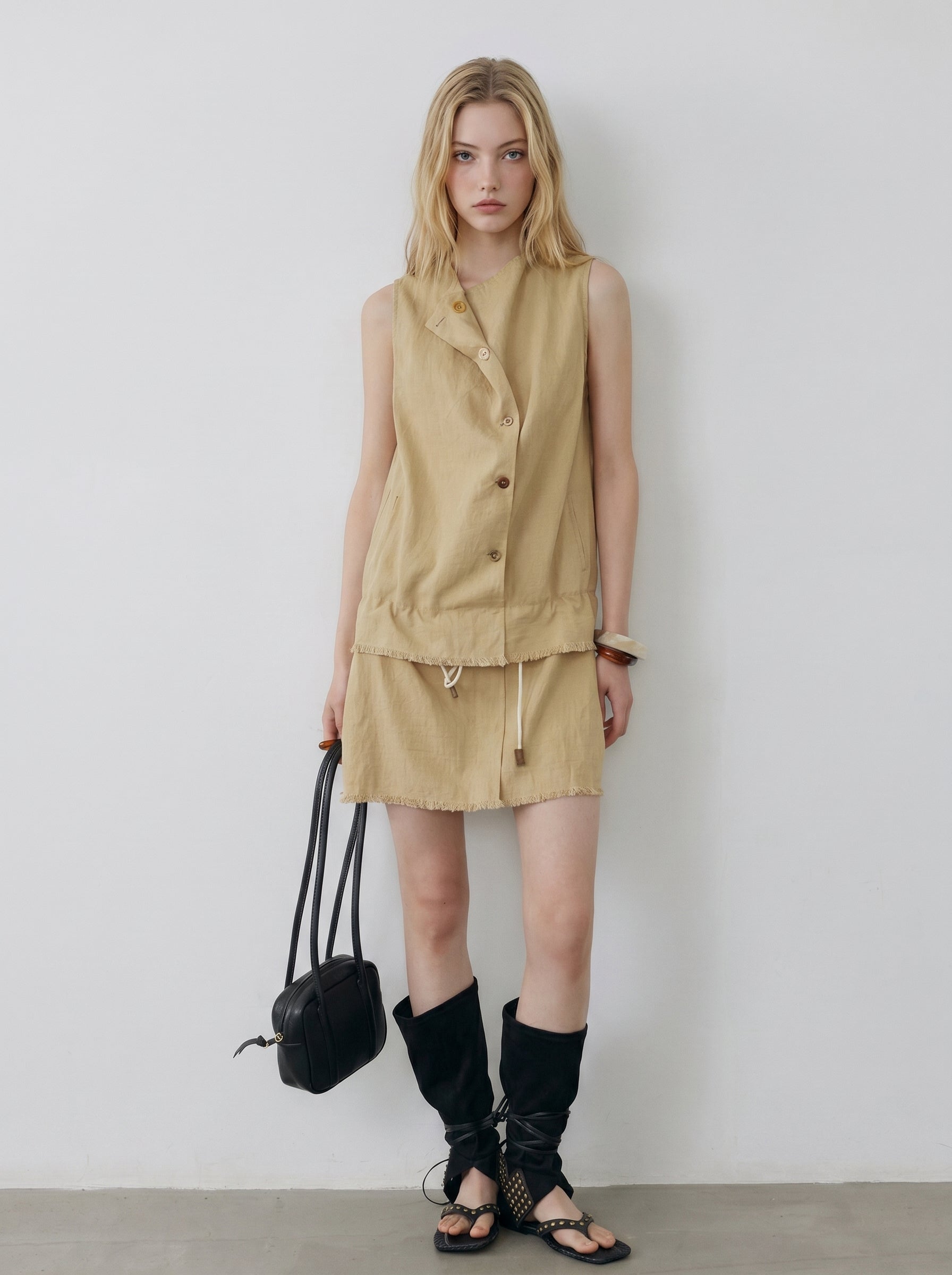 Beige sleeveless button-front mini dress with drawstring waist, styled with black boots and a black handbag