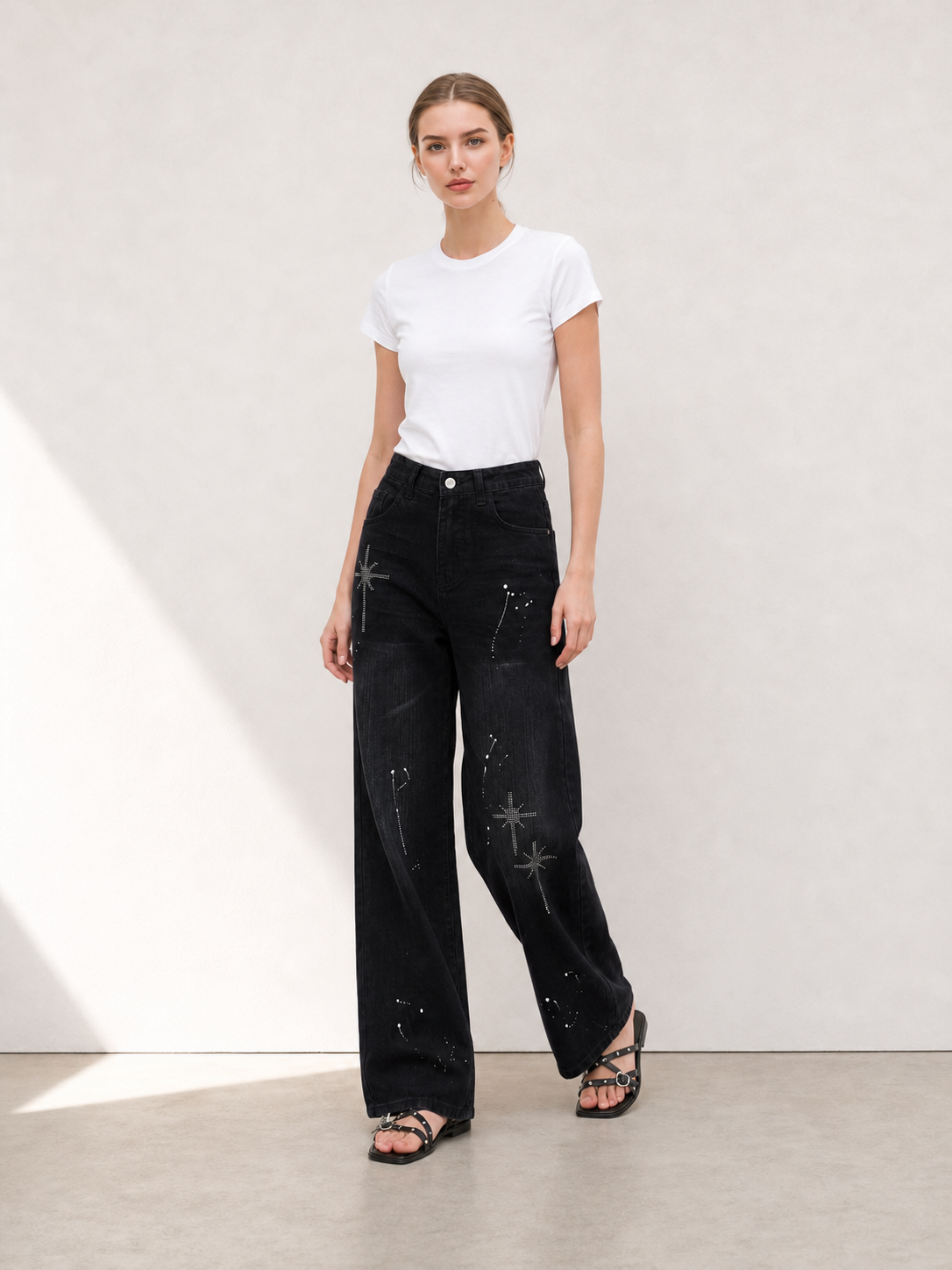 Front view of black rhinestone wide leg jeans styled with a white fitted T-shirt and black sandals
