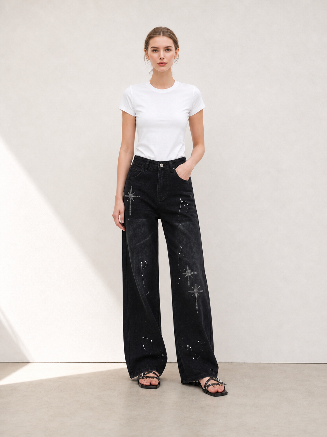Model wearing black rhinestone wide leg jeans with a white fitted T-shirt in a minimalist studio setting