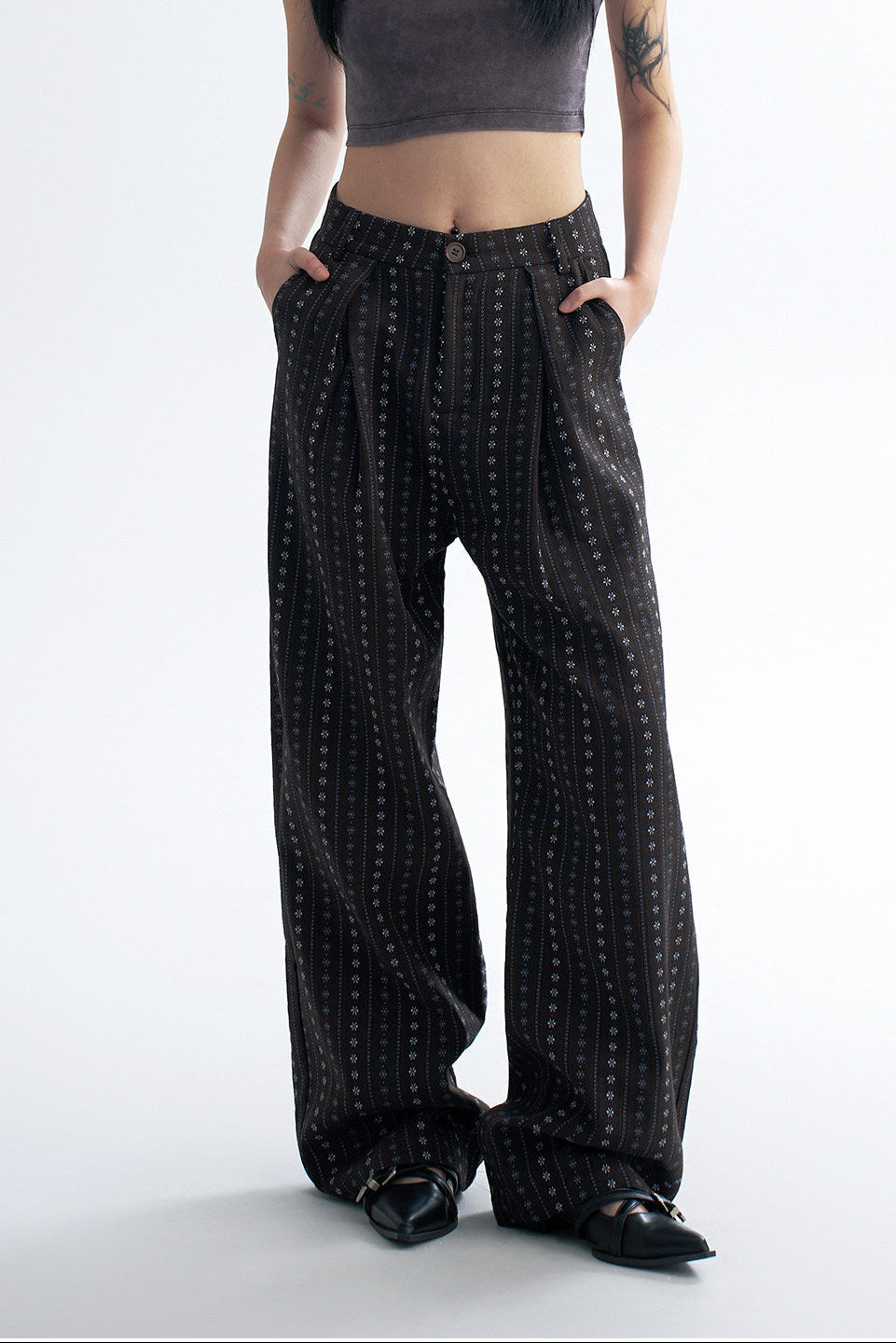 Close-up front detail of black striped wide leg pants showing the pleated waist, button closure, and vertical dot stripe pattern