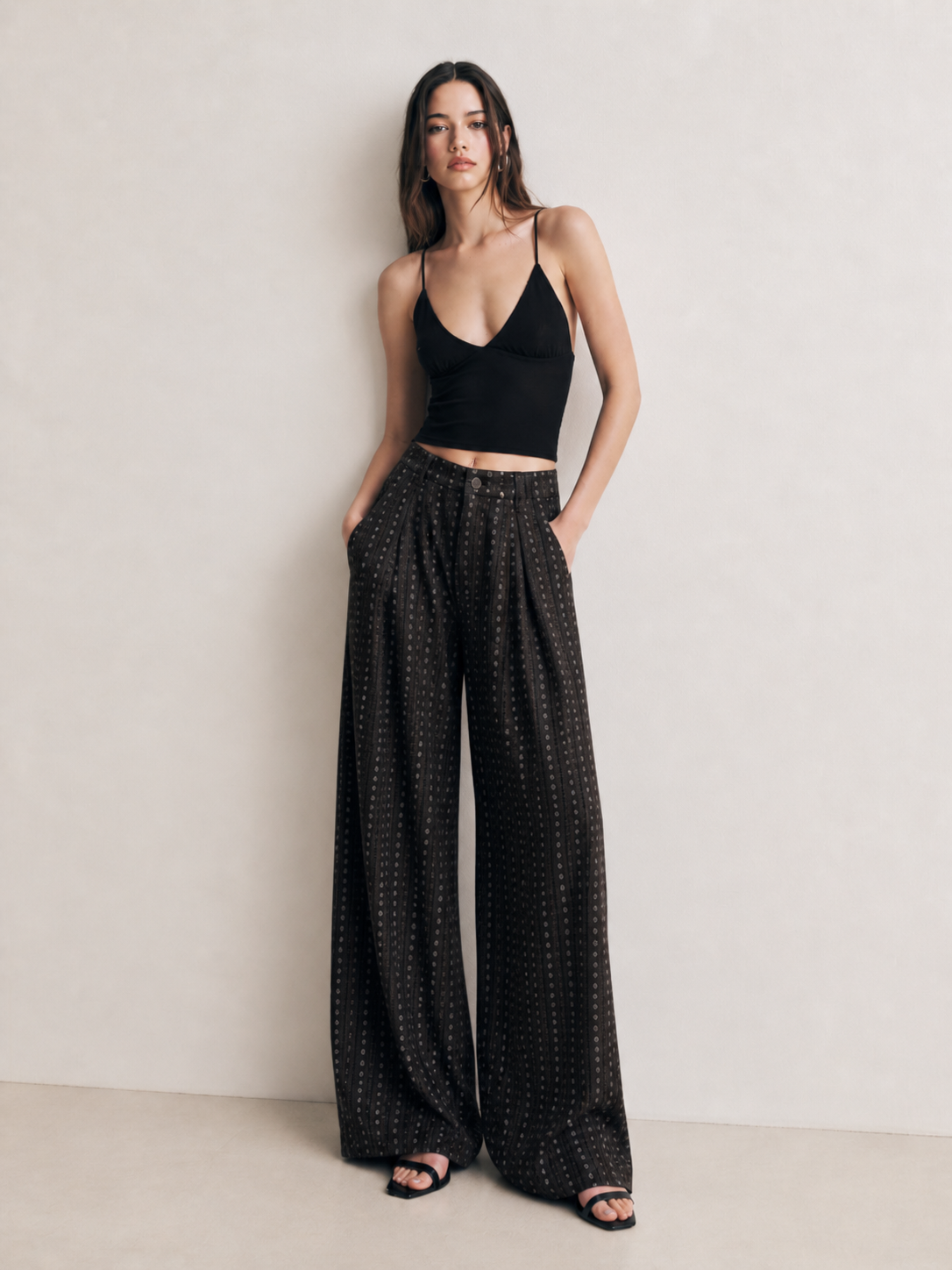 Model wearing black striped wide leg pants with a black strappy crop top against a minimalist neutral wall