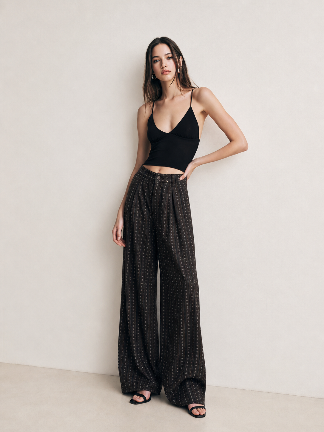 Black striped wide leg pants styled with a black crop top and heeled sandals in a minimal studio setting
