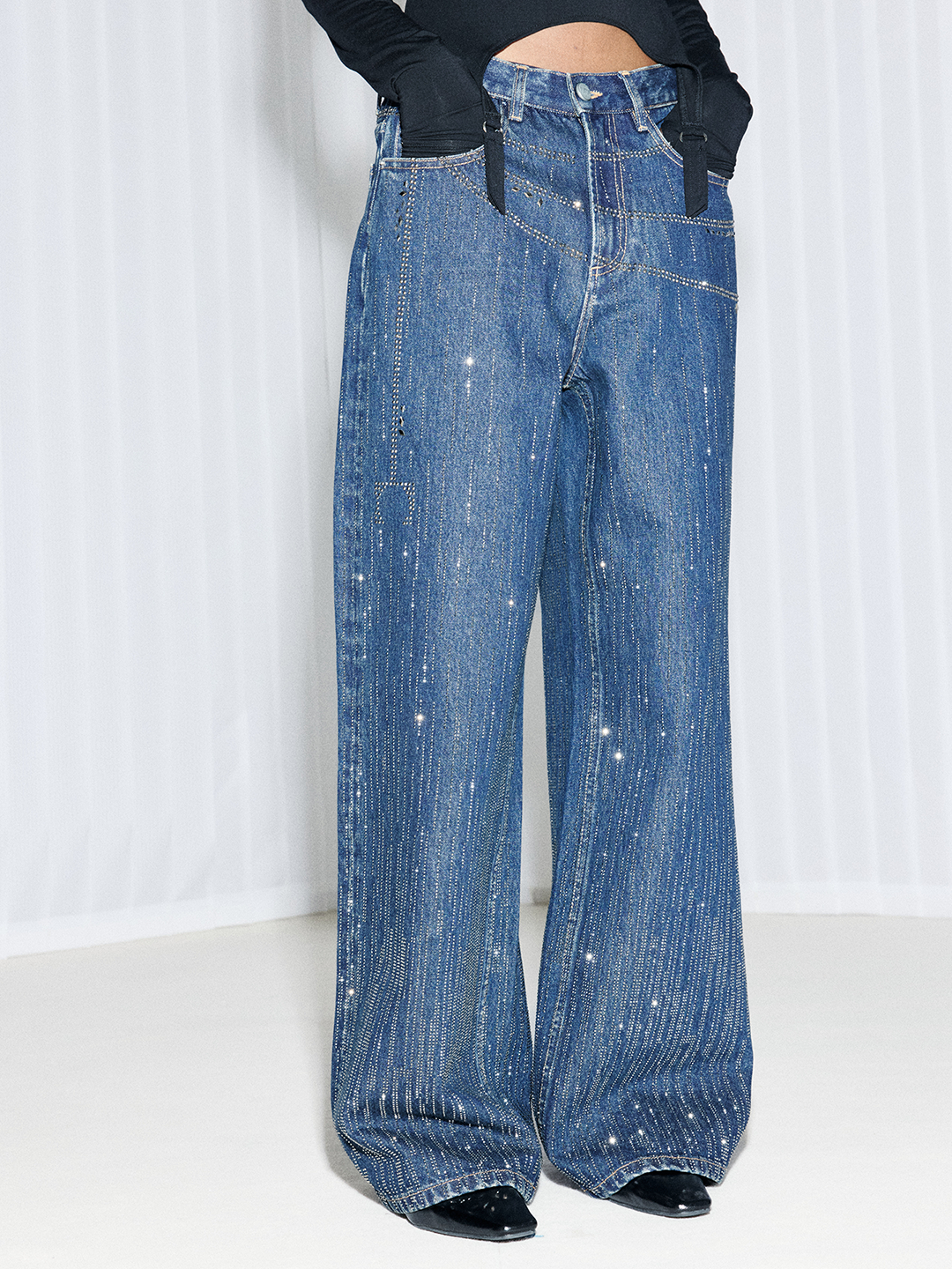 Front detail view of blue wide-leg jeans featuring sparkling rhinestone embellishments and oversized denim silhouette