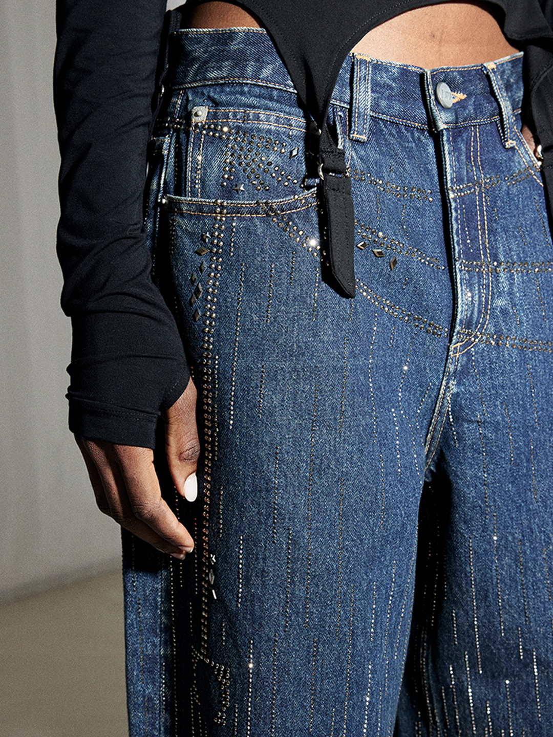 Close-up of blue jeans waistband, button closure, pockets, and rhinestone denim details