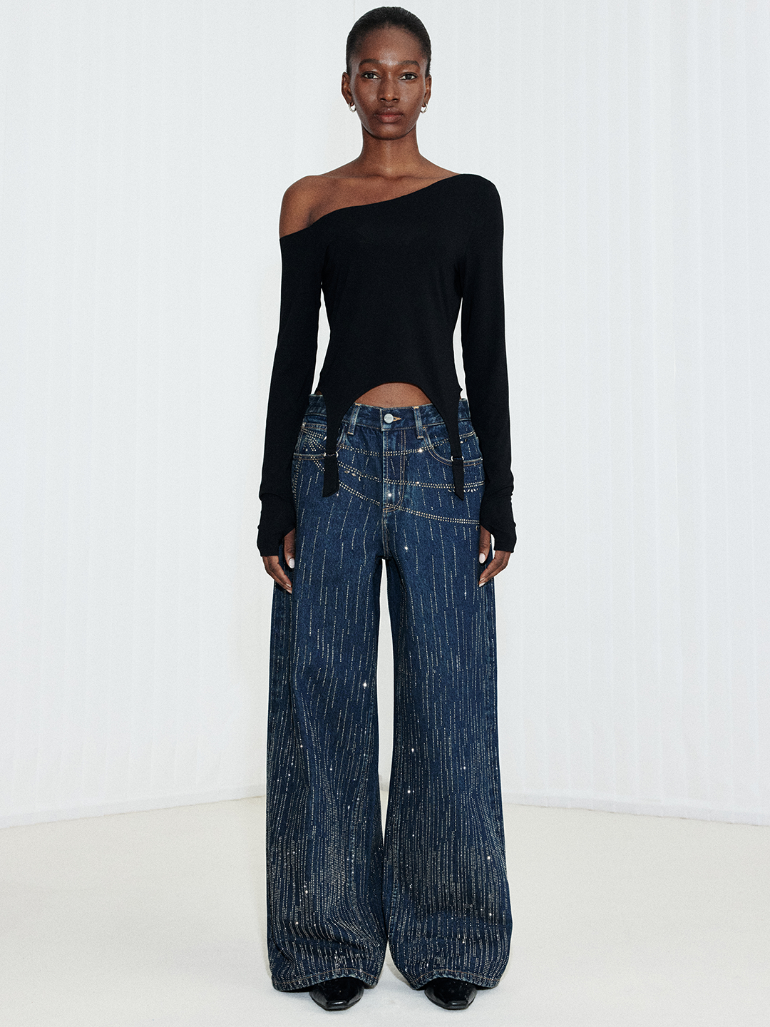 Model wearing blue wide-leg rhinestone embellished jeans with a relaxed fit and black off-shoulder top