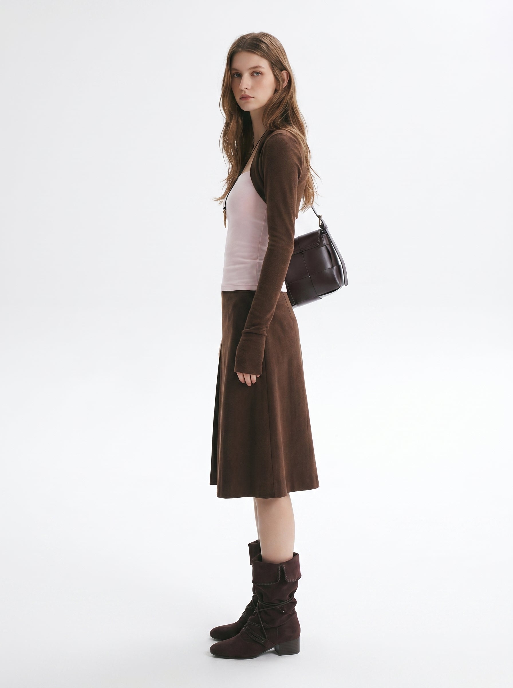 Side view of brown layered long sleeve top and matching midi skirt set styled with boots and a shoulder bag