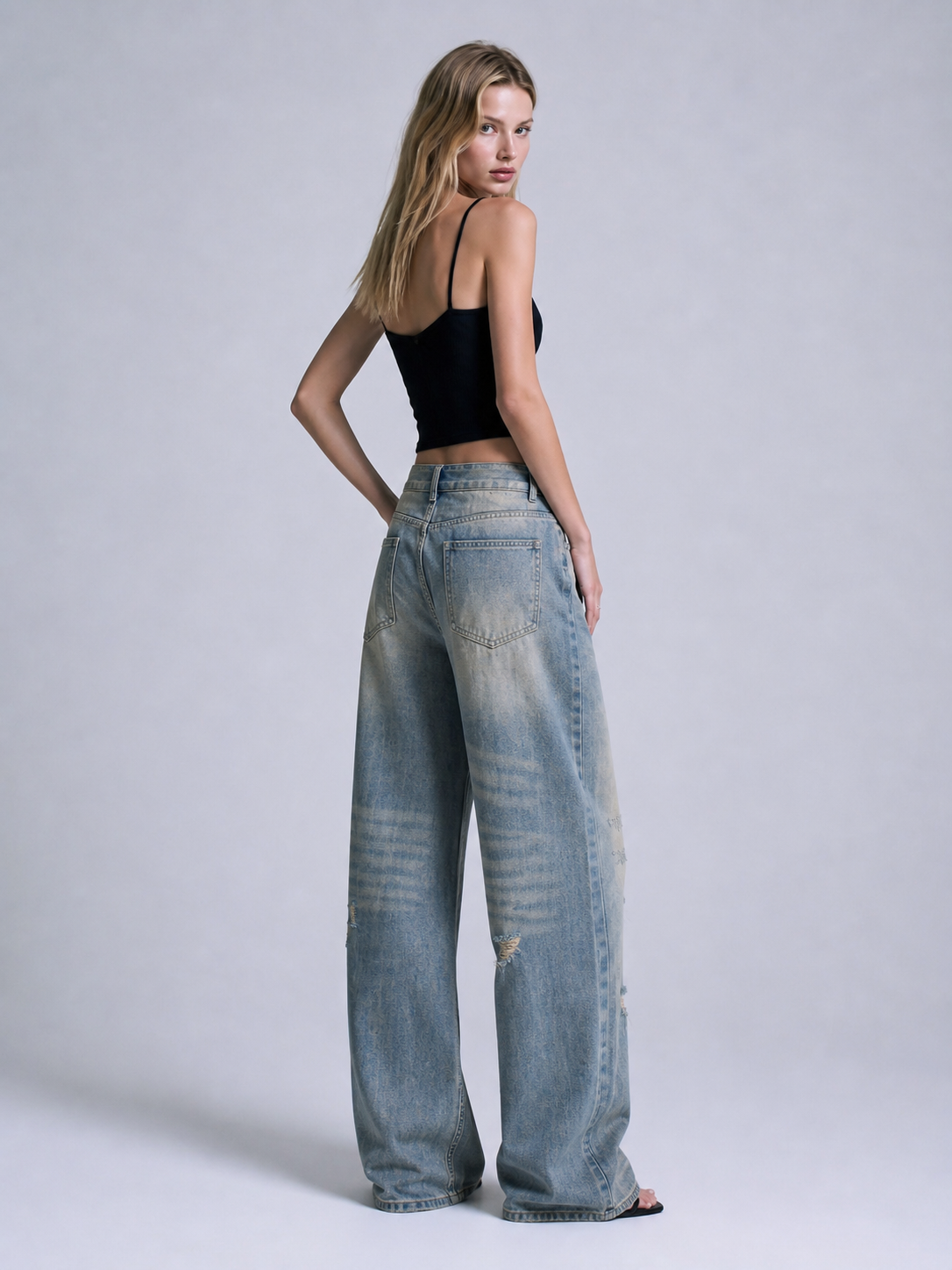 Back angled view of distressed blue wide leg jeans showing rear pockets, faded wash, and relaxed oversized fit