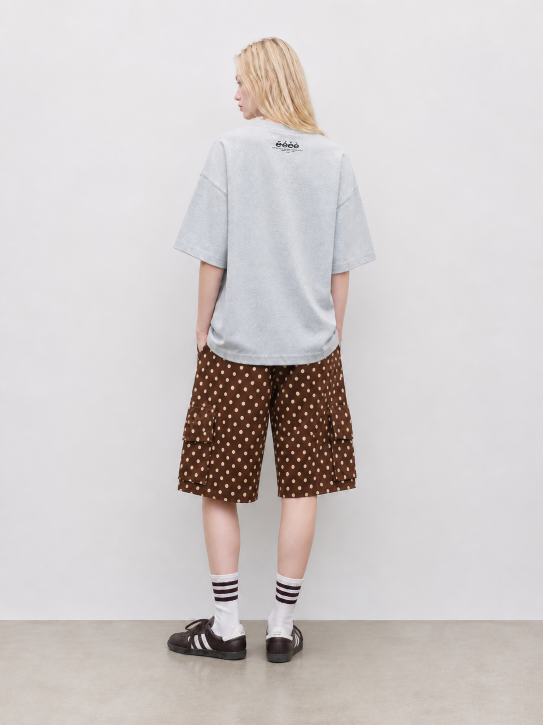 Back view of oversized gray T-shirt with brown polka dot cargo shorts, striped socks, and dark sneakers