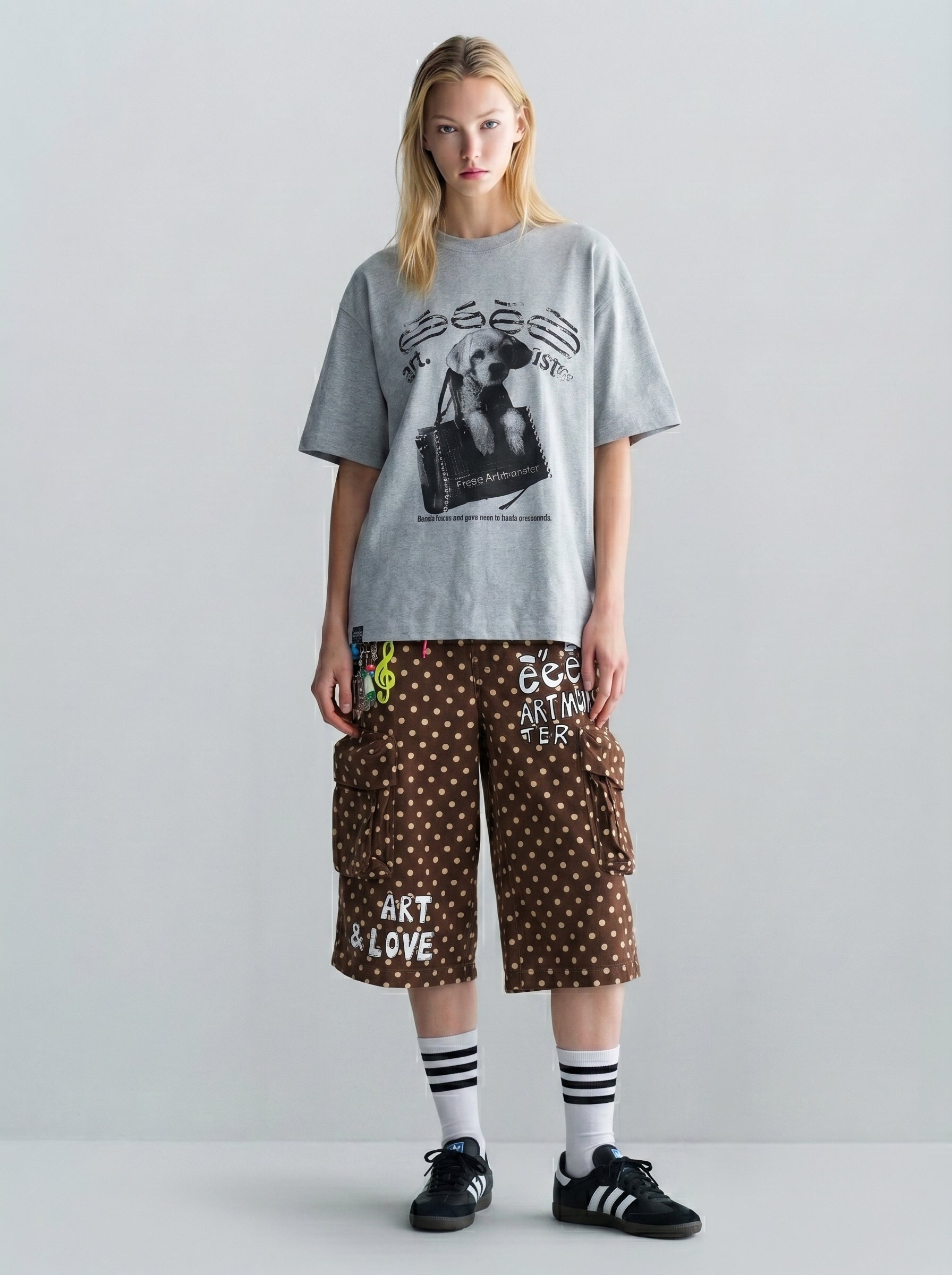 Oversized gray graphic T-shirt styled with brown polka dot cargo shorts, striped socks, and dark sneakers