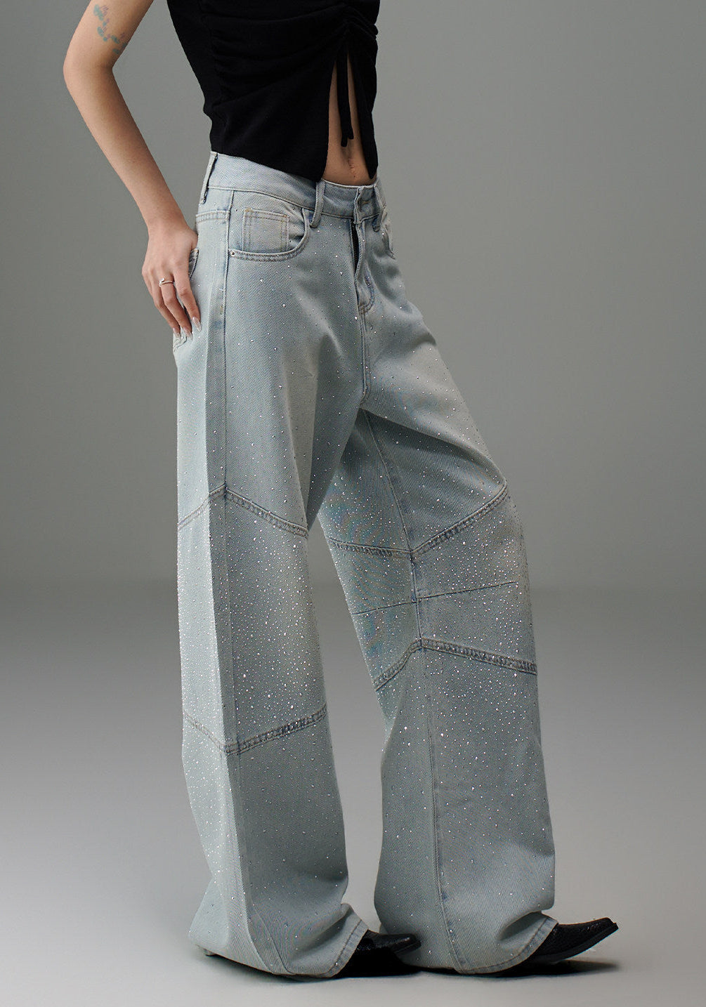 Angled detail view of light wash rhinestone wide leg jeans showing the curved seam panels and relaxed oversized fit