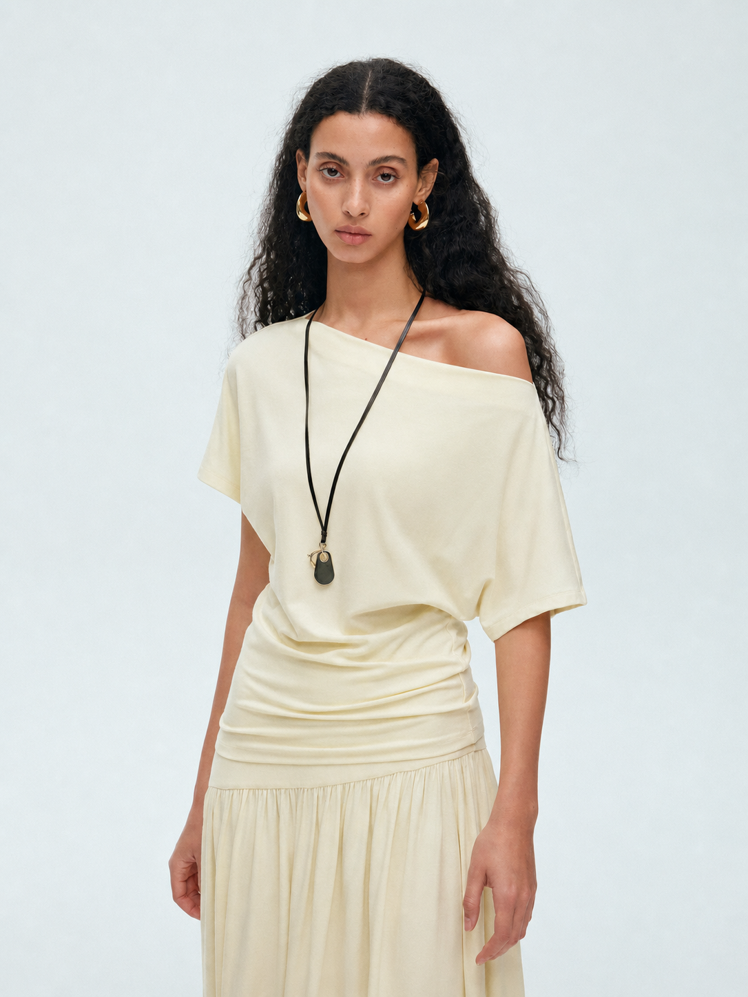 Model wearing a cream off shoulder draped top showing the relaxed neckline and soft waist drape