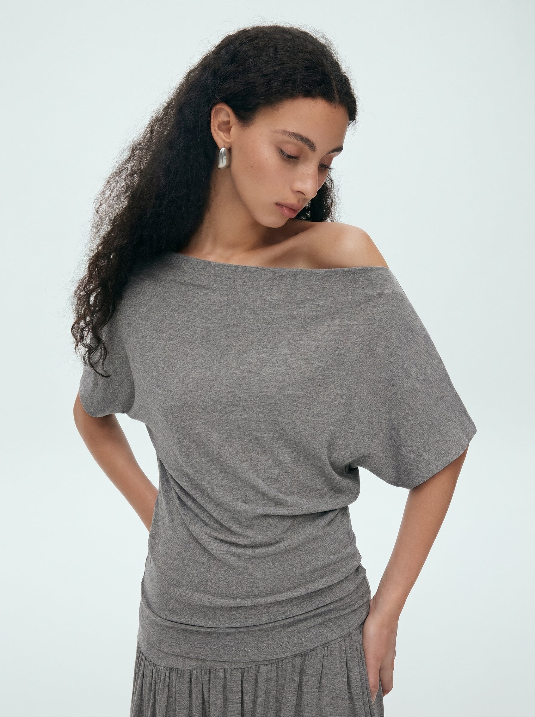 Close-up of grey off shoulder draped top showing the slouchy neckline and soft gathered waist