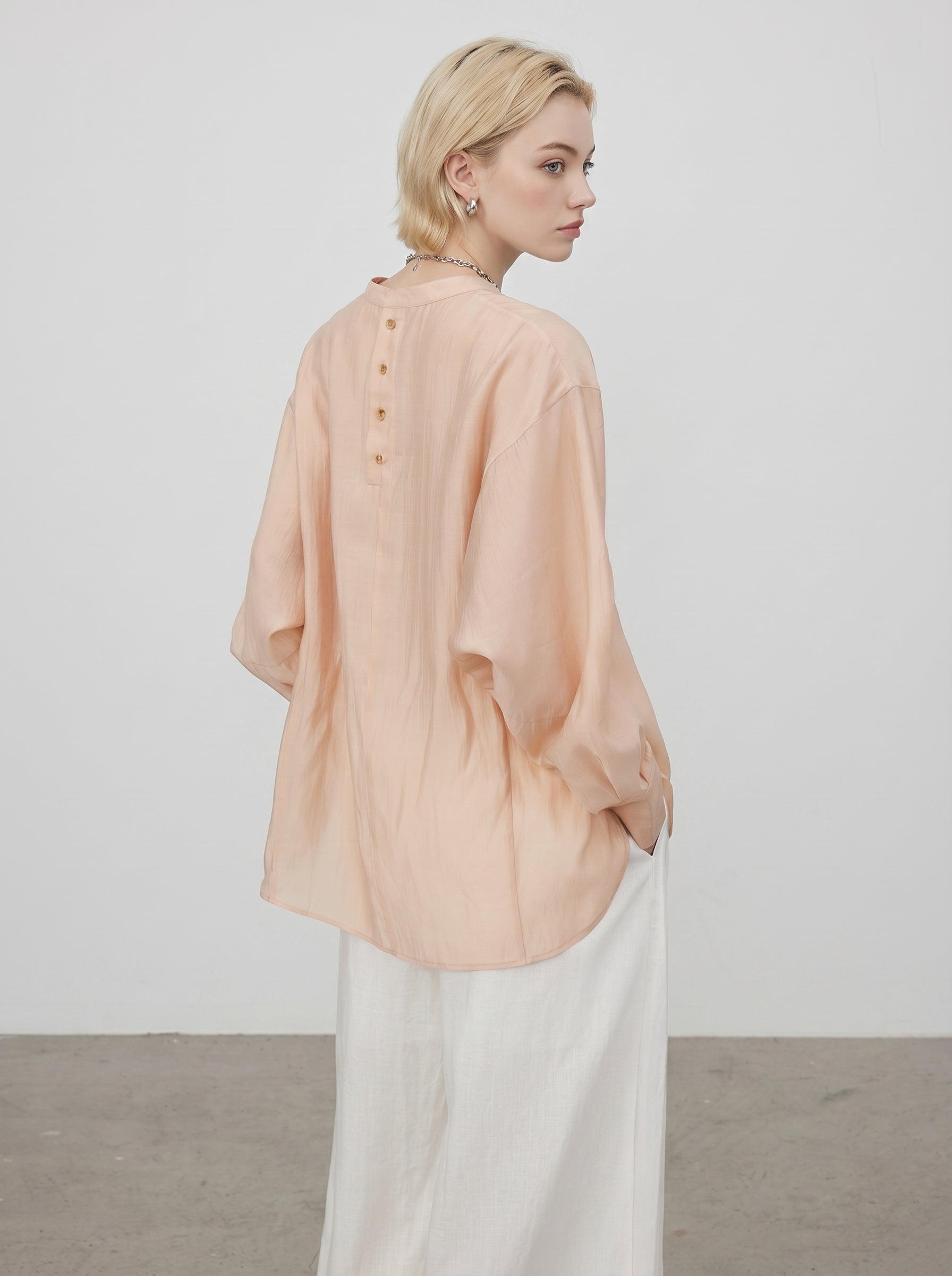 Back view of peach sheer blouse showing button details, relaxed long sleeves, and white wide leg pants