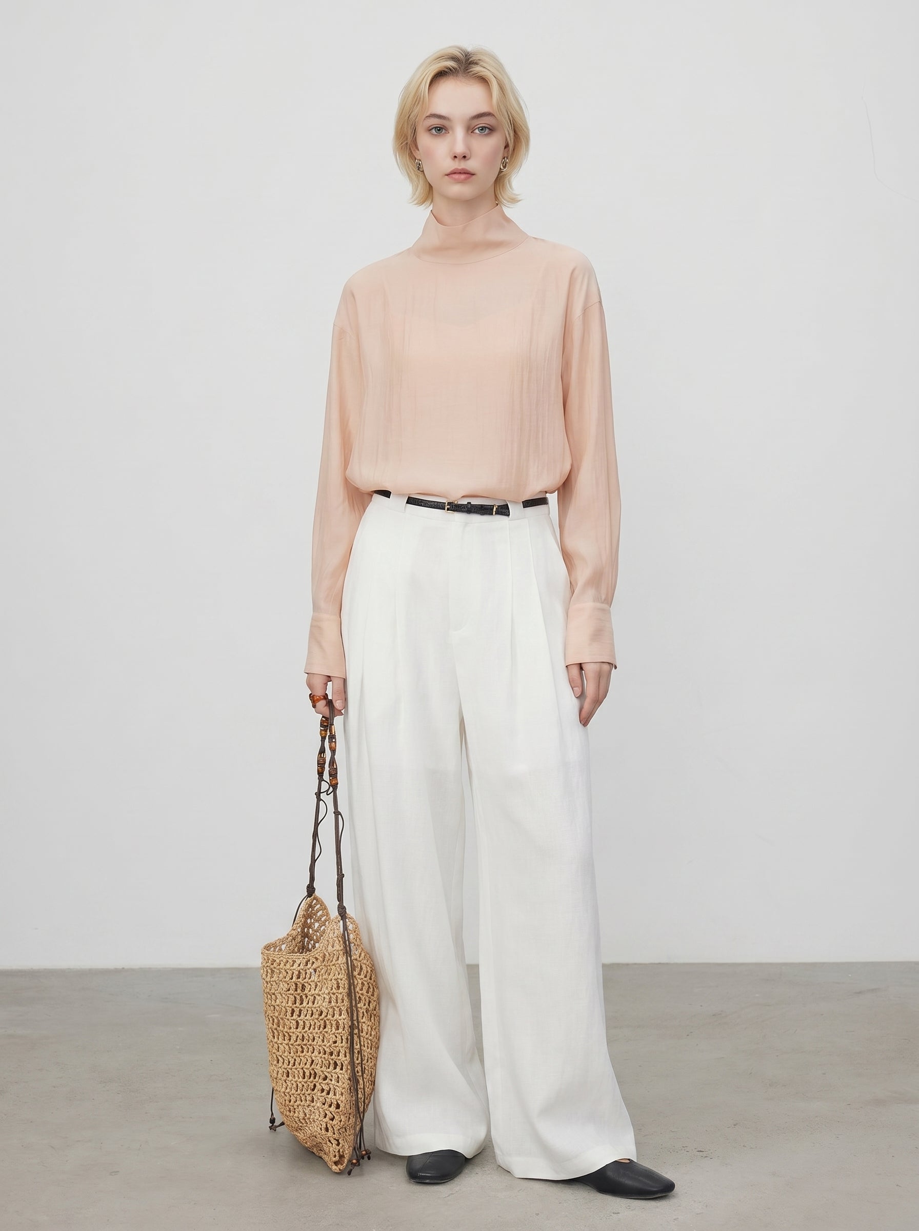 Peach sheer high neck blouse styled with white wide leg pants, black belt, and woven tote bag
