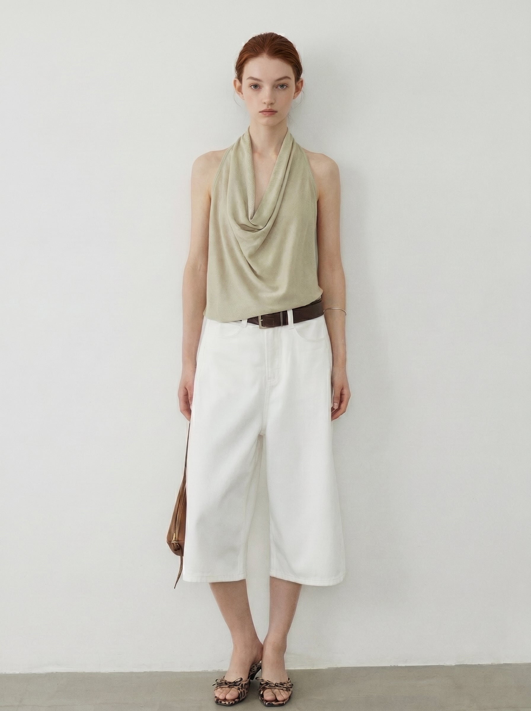 Full body front view of sage draped halter knit top with a cowl neckline and white wide leg pants