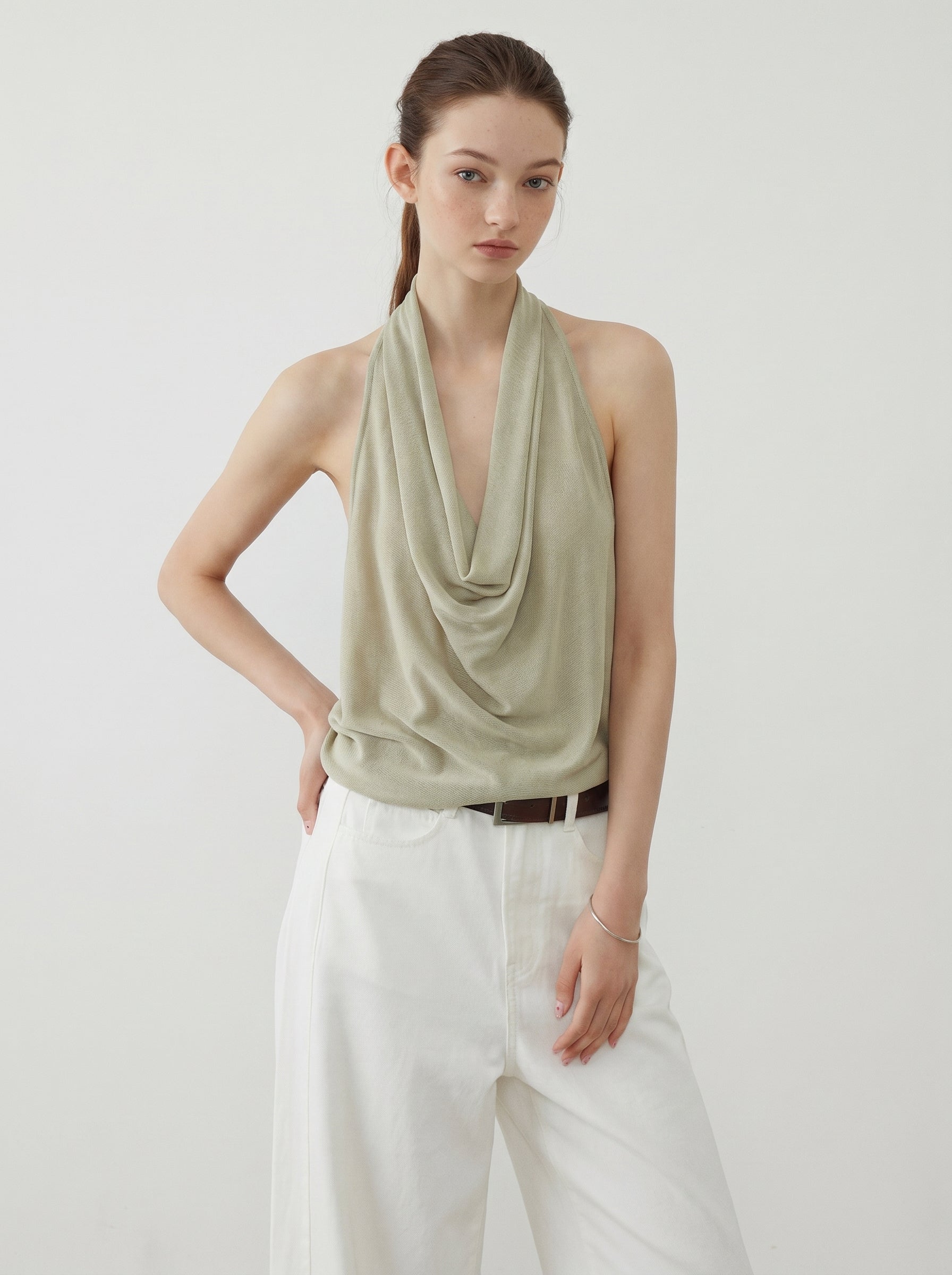 Sage draped halter knit top styled with white wide leg pants in a minimalist studio setting
