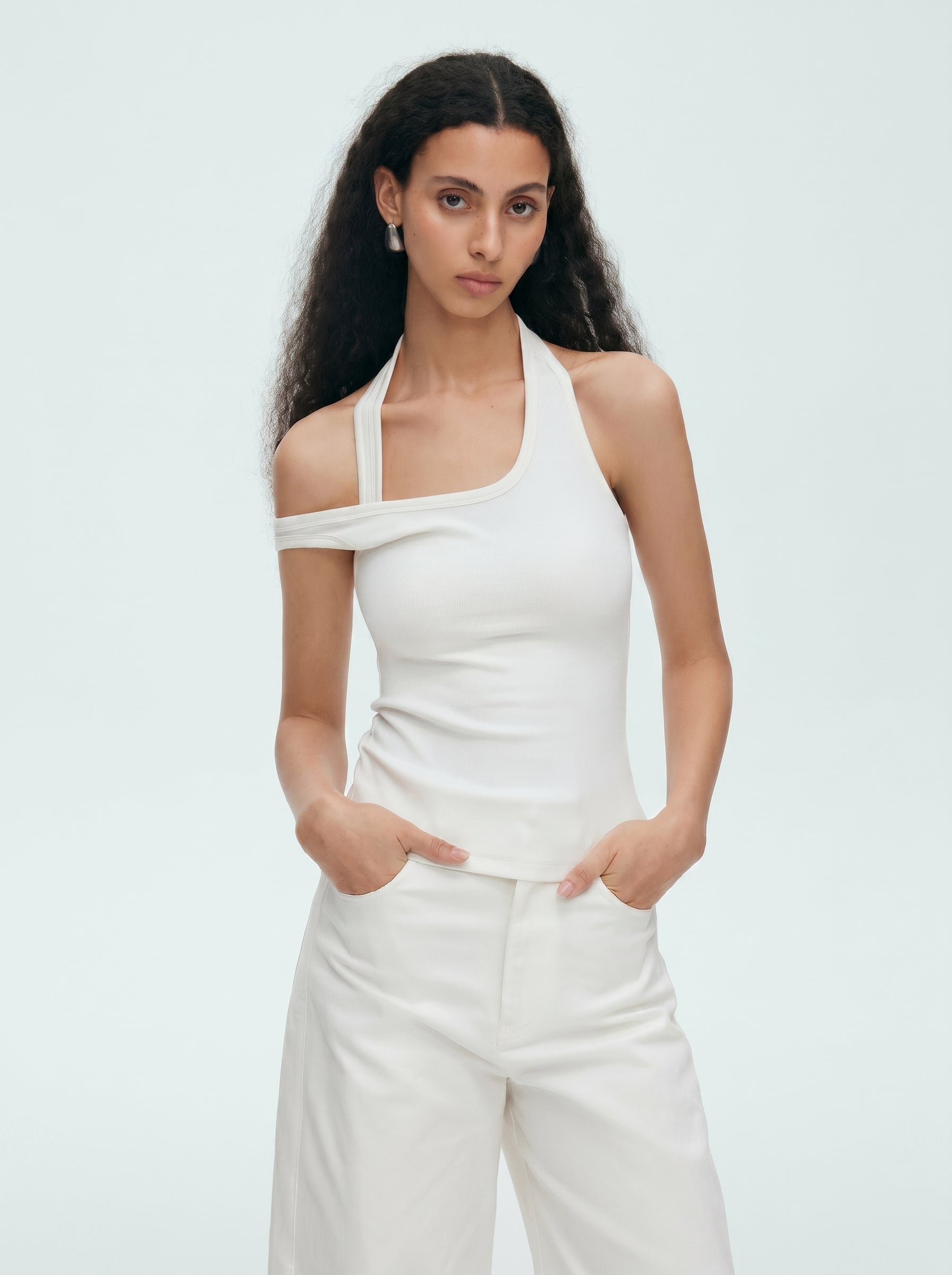 Model wearing a white convertible halter off shoulder top with white pants in a minimal studio setting